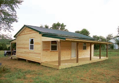 A finished Lucky house package with log siding, a green metal roof and a covered front porch
