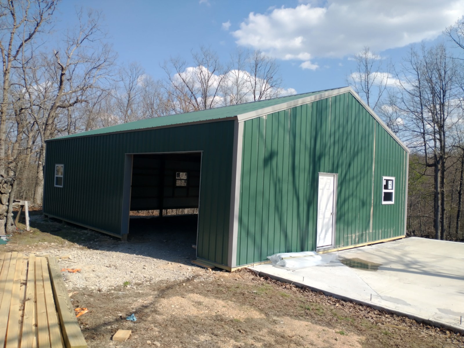 A green Lucky pole barn with a wide door opening, a walk door and windows