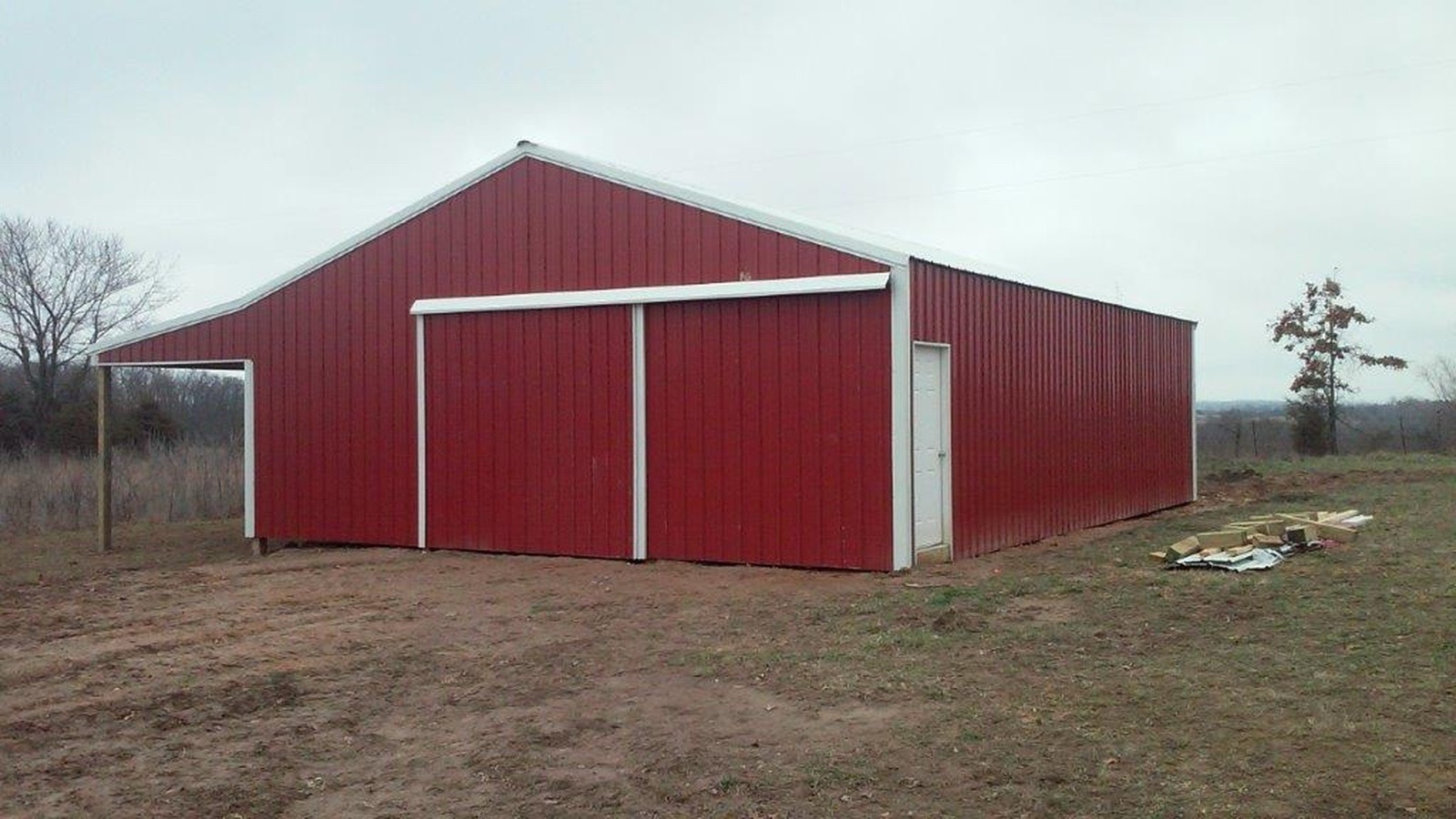 A red Lucky pole barn with white trim, sliding doors, a walk door and an open lean-to